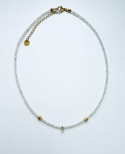 A necklace with moonstone all around and gold accents with a labradorite droplet in the center of the necklace. 