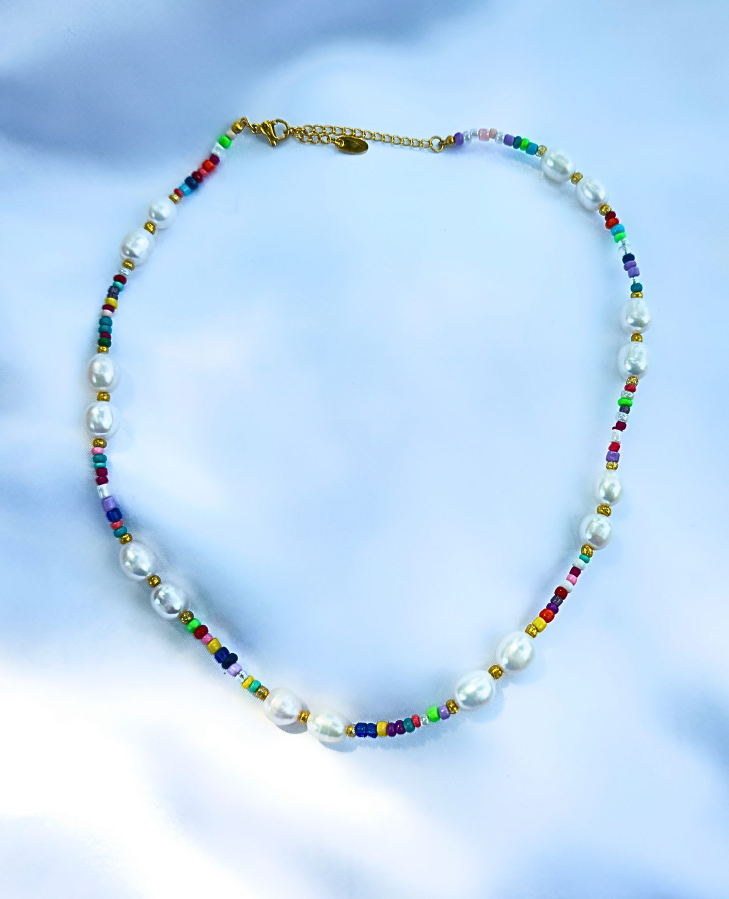 A necklace with multicolored beads mixed in with freshwater pearls layer on a silk fabric. 